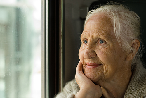 Senior woman wearing a cozy sweater smiling and looking out the window