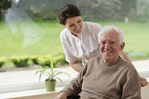 CNA in white scrubs standing behind smiling in wheelchair by a window